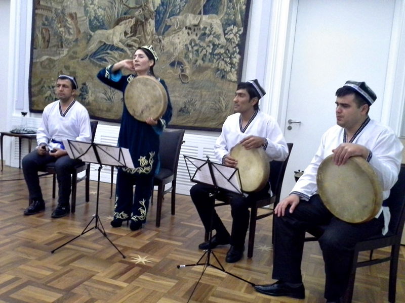 Reise nach Usbekistan vom 25. März bis 4. April 2019 Vier Musiker in traditioneller zentralasiatischer Kleidung, drei mit Rahmentrommeln und eine singende Frau, im Innenraum vor Wandteppich.