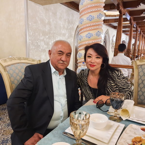 Reise nach Usbekistan 17. April - 27. April 2023 Älterer Mann im Anzug und Frau mit schwarzem Haar in elegantem Restaurant an gedecktem Tisch, dekorative Säulen im Hintergrund