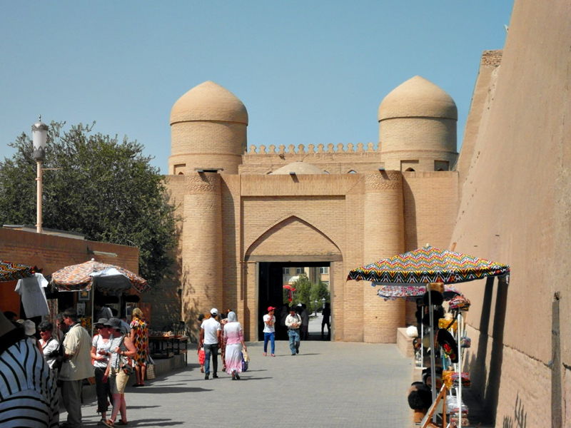Reise nach Usbekistan 11. April — 21. April 2016 Historisches Lehmmauer-Tor mit zwei runden Türmen und Basarständen davor, Touristen schlendern entlang der Promenade