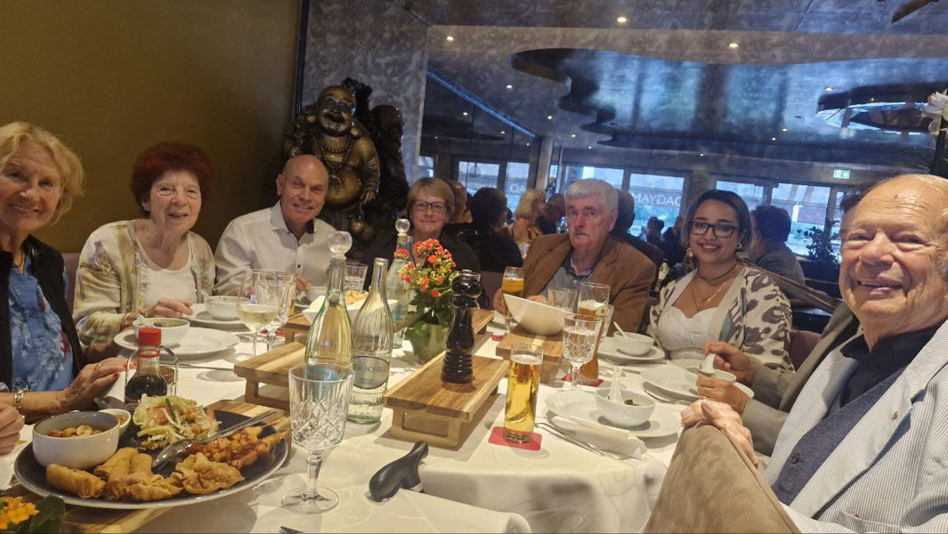 Seniorengruppe feiert gemeinsames Abendessen in Restaurant mit gedecktem Tisch, Getränken und asiatischen Vorspeisen