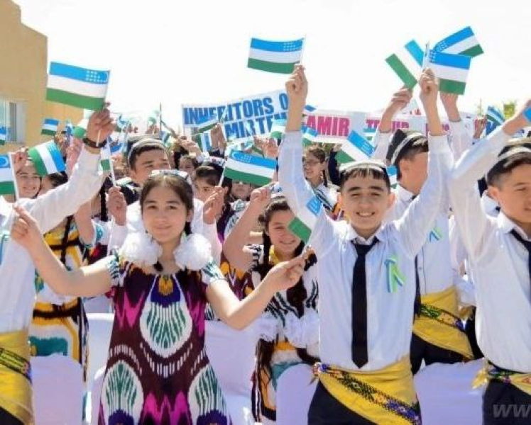 Schülerinnen und Schüler in traditioneller Kleidung und Schuluniform heben lächelnd usbekische Fahnen bei einer Feier im Freien