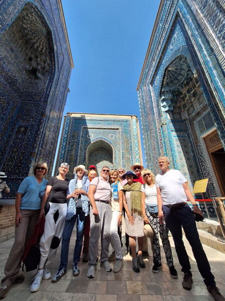 Reisegruppe vor blau-verzierten, islamischen Portalbauten mit Mosaiken und hohen Iwans unter klarem Himmel in Samarkand